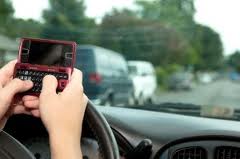 Person texting on a red flip phone with a QWERTY keyboard while driving, blurred traffic in background.