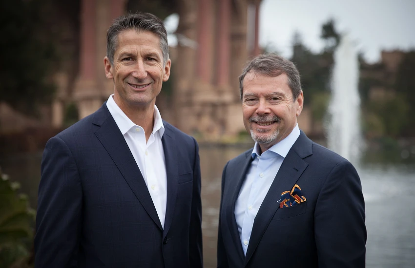 Community members smile in dark suits, posing outdoors by a fountain and classical architecture.