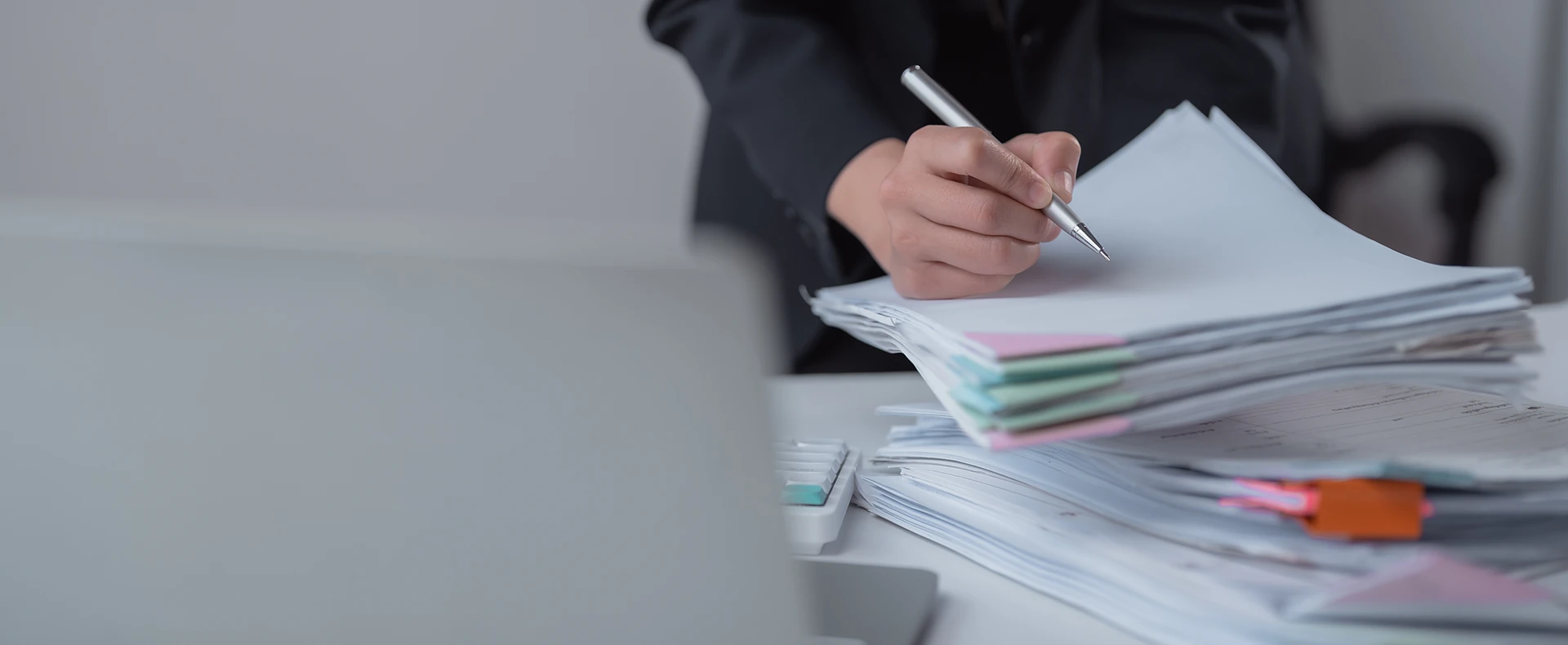 Person holding a pen over a large stack of legal case files and documents representing a mass tort claim